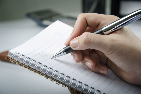 A pen is poised over a notepad for meeting transcription