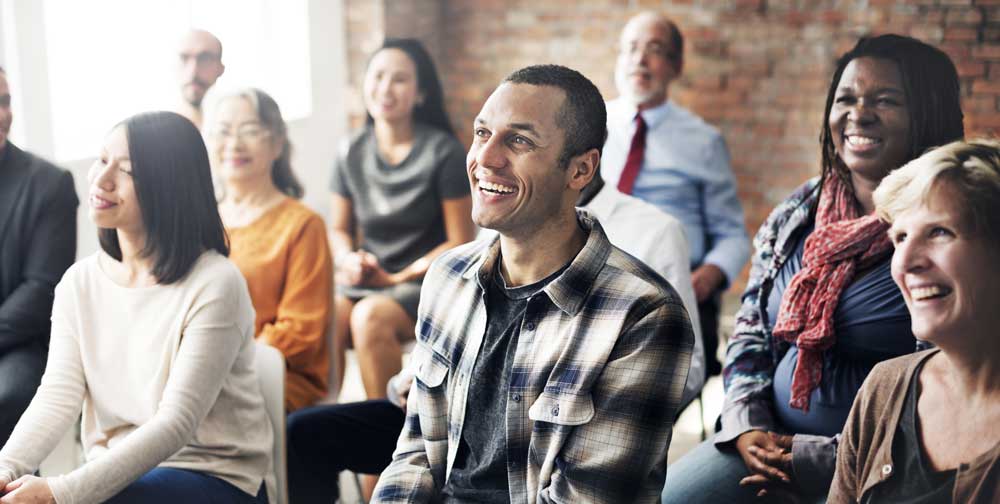 A group of people sit in a meeting, smiling