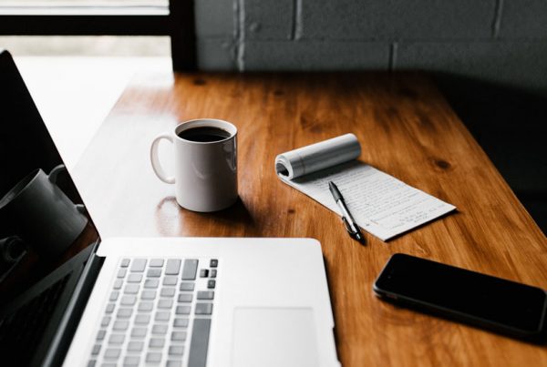 desk with laptop, phone, notebook and coffee representing remote working