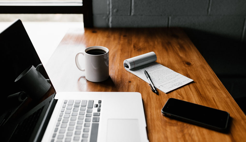 desk with laptop, phone, notebook and coffee representing remote working